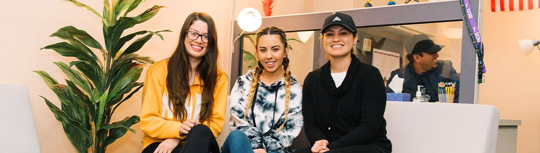 three students sit on a couch smiling in a Pima student services center